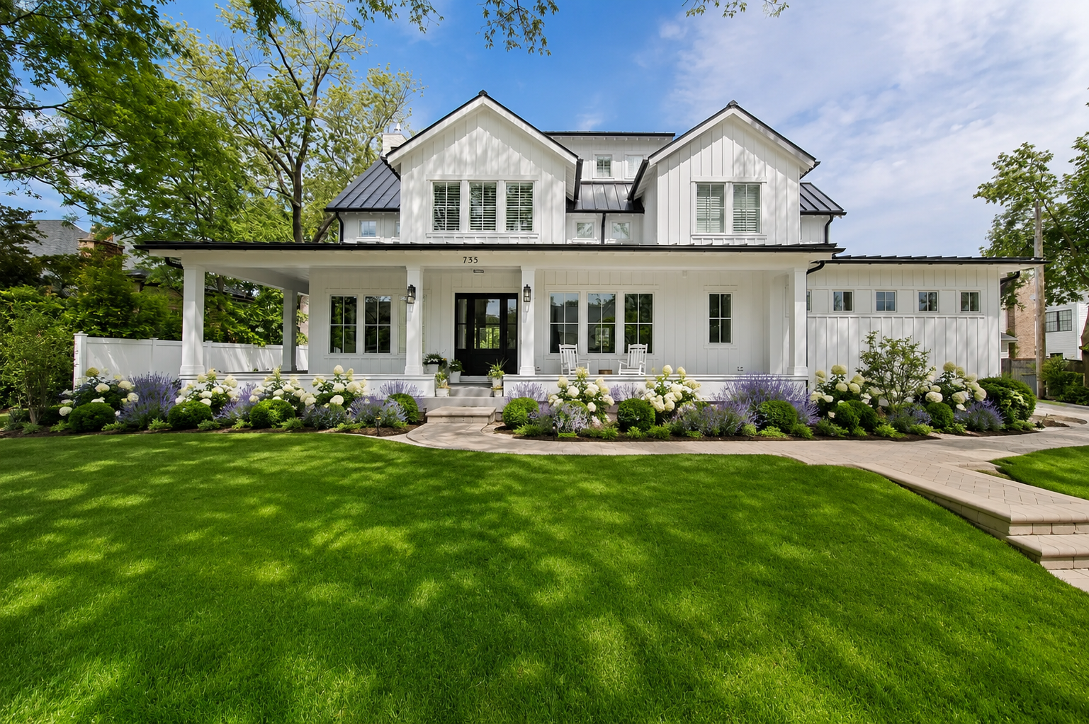 Front exterior of the custom-built modern farmhouse with wrap-around porch and lush landscaping