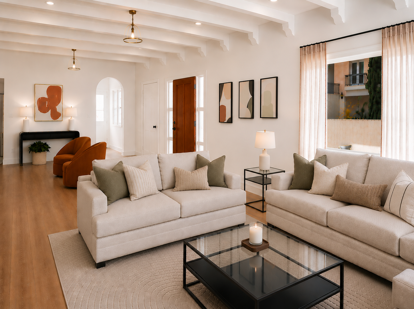 Main living room with original exposed ceiling beams, arched entry door, wide-plank oak floors, and neutral furnishings with terracotta and sage accents